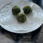 Small white plate with 3 cooked spinach bites on a dark granite counter.